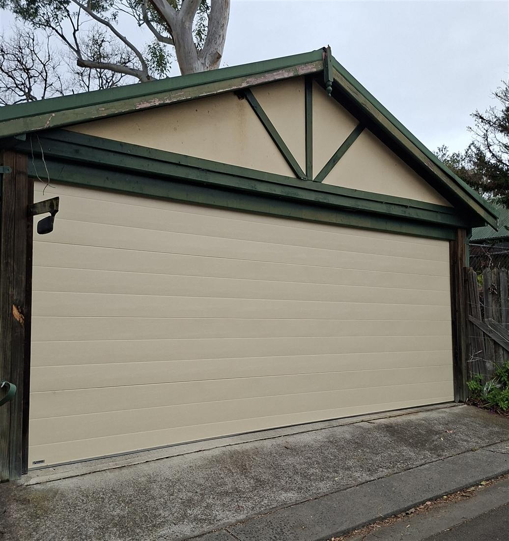 Cream sectional garage door installation with green roof trim